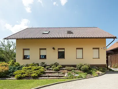 Rodinný dům s uzavřenými venkovními roletami na oknech a upravenou předzahrádkou