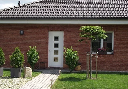 Bílé vstupní dveře se skleněnými čtvercovými výplněmi na cihlovém bungalovu